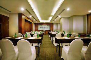 雅加达ASTON Pluit Hotel & Residence的餐厅设有桌子、白色椅子和屏幕
