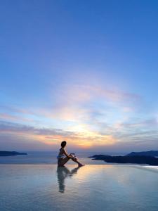 费拉Lilium Hotel Santorini的坐在水中观看日落的人