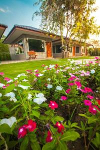 南府Villa De Bua Resort Nan的一座花园,在房子前方种有粉红色和白色的花朵