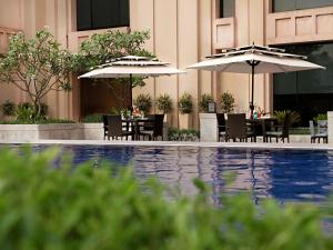 新德里新德里大都市温泉酒店的池畔餐厅,配有桌子和遮阳伞