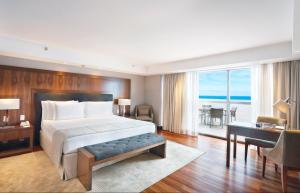 里约热内卢Windsor Marapendi Hotel的一间卧室配有一张大床和一张书桌,另一间房间享有美景。
