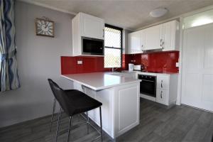 新月岬Beachfront 3, 25 Willow Street的厨房配有红色和白色的橱柜和黑椅