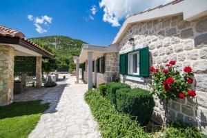 Duge NjiveVilla Silentio, complete privacy near Makarska的一座石头房子,设有绿色的窗户和红色的玫瑰