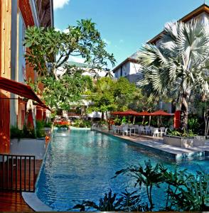 库塔落日余晖大道哈里斯度假酒店的一座带桌子和遮阳伞的游泳池位于一座建筑旁边