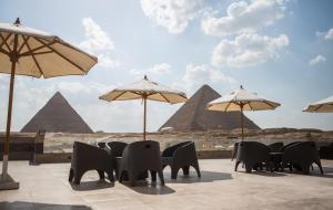 开罗Hayat Pyramids View Hotel的一个带椅子和遮阳伞及金字塔的庭院