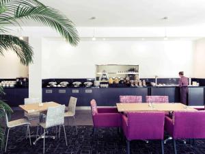 纽卡斯尔纽卡斯尔机场美居酒店的餐厅设有桌子和紫色椅子,厨房设有厨师