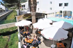 圣港普拉亚多拉达酒店的坐在桌边的游泳池边,有遮阳伞的人