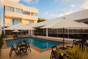 马卡帕ROYAL Hotel & Gastronomia的一座带桌子和遮阳伞的游泳池位于一座建筑旁边