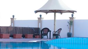 锡卜Remas Hotel Suites - Al Khoudh, Seeb, Muscat的一组椅子和一把遮阳伞,位于游泳池旁