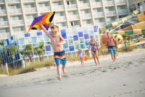 默特尔比奇皇冠珊瑚礁海滩度假村及水上乐园的一名小男孩带着风筝在海滩上跑