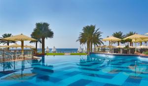 阿吉曼巴希阿治曼宫酒店 的一个带遮阳伞和海洋的游泳池