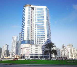 沙迦阿雅那酒店的一座高大的建筑,在城市前方有一棵棕榈树