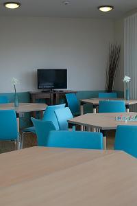 柏林CVJM Jugendgästehaus Berlin的客房设有桌子、蓝色椅子和平面电视。