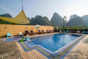 阳朔阳朔格格树饭店的一个带椅子和遮阳伞的游泳池,背景是山脉
