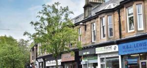 米尔盖West Highland Apartments Milngavie - The Lomond的一条街道,在一座建筑前有商店和树