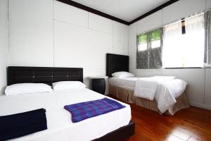 古晋绿色小屋民宿的卧室设有两张床,拥有白色的墙壁和木地板
