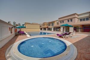 迪拜J5 Villas Holiday Homes Barsha Gardens的一座带椅子和遮阳伞的游泳池位于一座建筑旁边