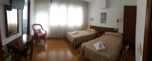VimianzoPensión Vázquez的酒店客房设有两张床、一张桌子和一张书桌。