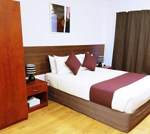 奥克兰机场花园会议中心酒店的一间卧室配有一张大床和木制床头板