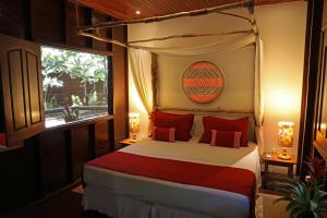 马瑙斯亚马逊生态园丛林旅馆的一间卧室配有一张带红色枕头的天蓬床和窗户。