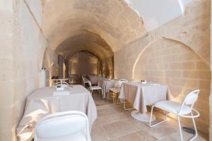 马泰拉Aquatio Cave Luxury Hotel & SPA的石头建筑中一间设有白色桌椅的餐厅