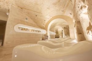 马泰拉Aquatio Cave Luxury Hotel & SPA的石墙内带白色椅子的房间