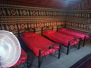 瓦迪拉姆Climbers House in Wadi Rum的客房设有3张红色的床和风扇。