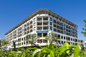凯恩斯曼特拉滨海酒店的一座白色的大建筑,前面有棕榈树