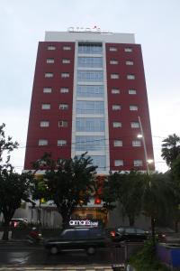 泗水爱玛瑞丝泗水马格雷酒店的一辆公共汽车驶过高高的红色建筑