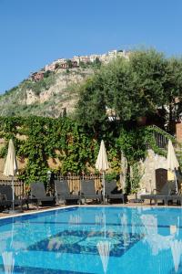 陶尔米纳安吉拉别墅酒店的山边带椅子和遮阳伞的游泳池