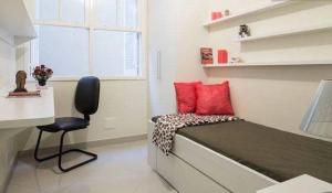 阿雷格里港Suítes e Quartos na Avenida Carlos Gomes的小房间设有一张带红色枕头的床和一把椅子