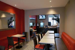 Aunay-sur-OdonLOGIS -Hotel & Restaurant de la Place的一间有红色墙壁和桌子的餐厅,一个坐在柜台上的人