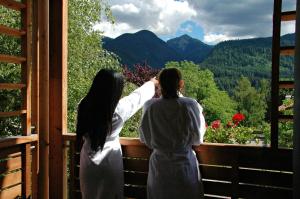菲耶梅堡奥利派尼克酒店的两名妇女站在一个眺望着山脉的阳台