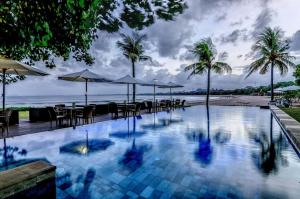 库塔巴厘岛花园海滩假日酒店的毗邻大海的带桌子和遮阳伞的游泳池
