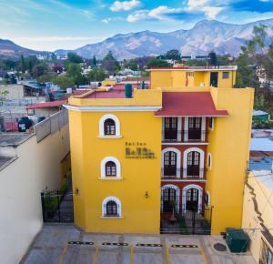 瓦哈卡市Suites Bello Xochimilco by DOT Tradition的一座黄色建筑,有红色屋顶,背景是群山