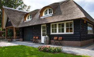 Sint MaartensbrugVilla Mare的黑色小屋,设有茅草屋顶和椅子
