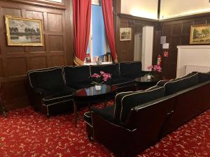 维也纳斯科顿托男爵膳食公寓酒店的一间设有黑色沙发和桌子的等候室,铺有红色地毯