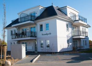 伯尔格伦德-雷特维施Fewo Strandleben Haus Strandperle的白色的建筑,有黑色的屋顶