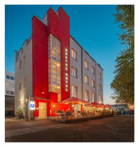美因河畔法兰克福Goethe Hotel Messe by Trip Inn的一座红色的建筑,前面设有桌子和遮阳伞