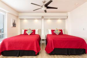 曼哈顿海滩海景海滩假日酒店的宿舍间的两张床,配有红色床单和吊扇