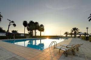 贝尼卡洛贝尼卡洛旅馆的一个带长椅和棕榈树的游泳池,并可欣赏日落美景