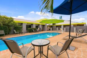 赫维湾赫维主湾康夫特汽车旅馆的一个带椅子和桌子的游泳池以及一把遮阳伞