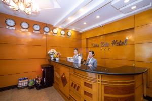 胡志明市Bon Ami Hotel - Thiên Xuân Hotel的两个人站在一个有时钟的房间的柜台上