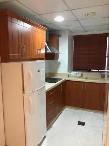 沙迦Al Majarah Residence的厨房配有木制橱柜和白色冰箱。