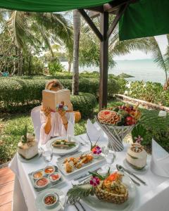 波普托Bo Phut Resort and Spa - SHA Plus的坐在餐桌旁一边读书一边吃着食物的女人