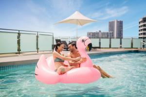 黄金海岸voco Gold Coast, an IHG Hotel的坐在游泳池里的粉红色火烈鸟的男人和女人