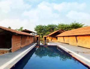 塔拉Maati Jungle Lodge Resort Bandhavgarh的两栋小屋之间享有游泳池的景致