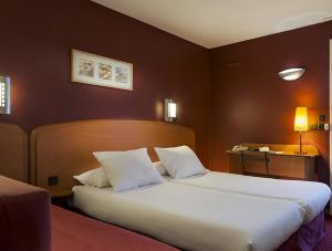 古桑维尔Sky Hotel Goussainville Charles de Gaulle的酒店客房配有一张带白色枕头的大床