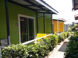 桑卡武里Sripech Home的绿色的房子,设有黄色和绿色的窗户和灌木丛