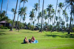 库德岛阁骨岛海滩度假酒店的两个人坐在棕榈树公园的草地上